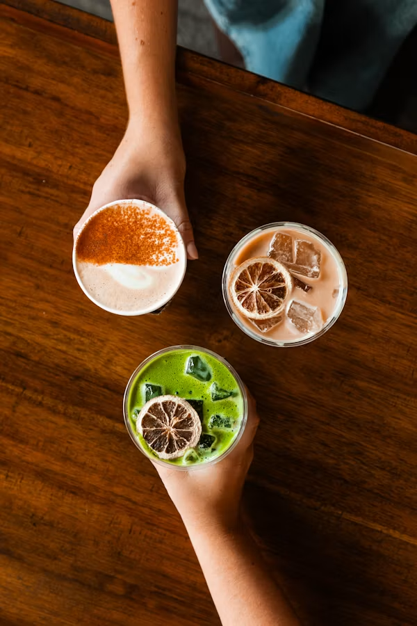 Overhead photograph of three drinks on a warm wooden table
