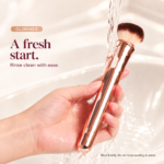 Glimmer rose-gold brush vibrator held under a gentle stream of water for a brief rinse.