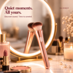 Glimmer rose-gold brush vibrator leaning against a round vanity mirror beside a candle and pearls.